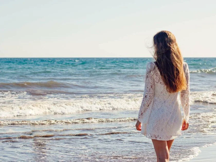 woman on beach wearing white dress with long brunette hair