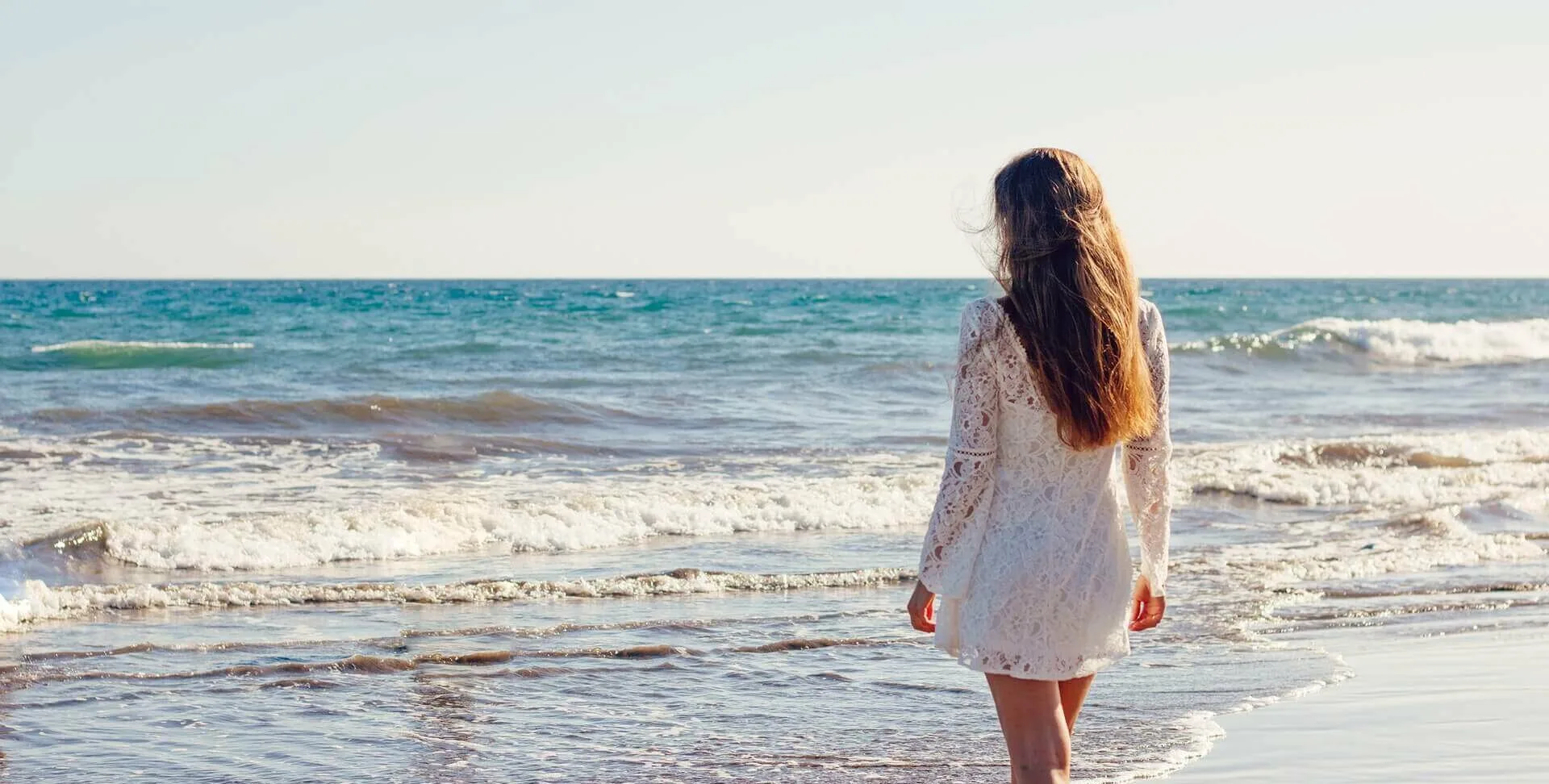 woman on beach wearing white dress with long brunette hair